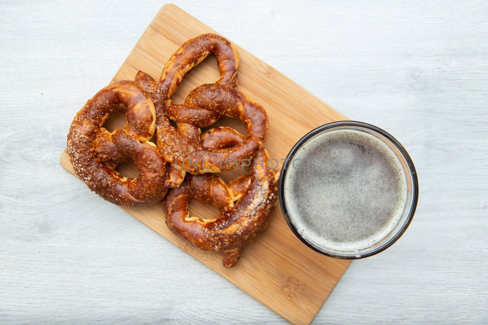 Freshly baked homemade soft pretzel with salt on wooden cutting board with glass of beer. by marynkin