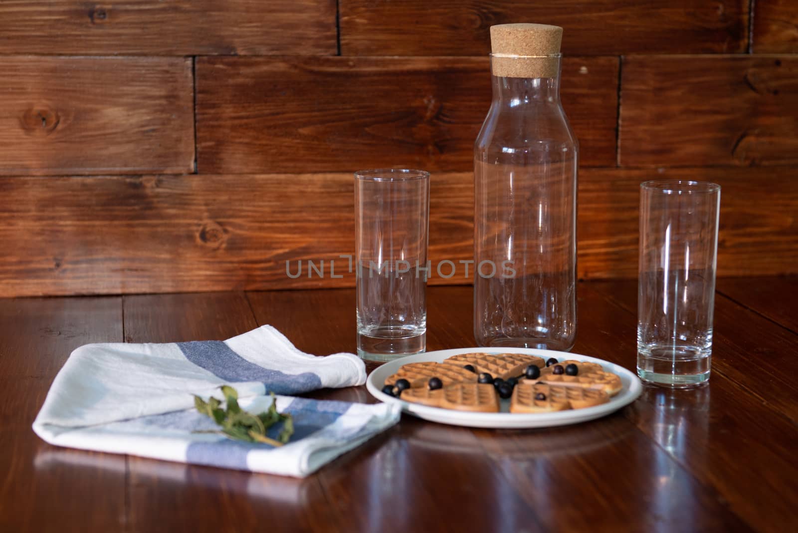 an empty bottle, two glasses and wafers on a plate. Wooden background