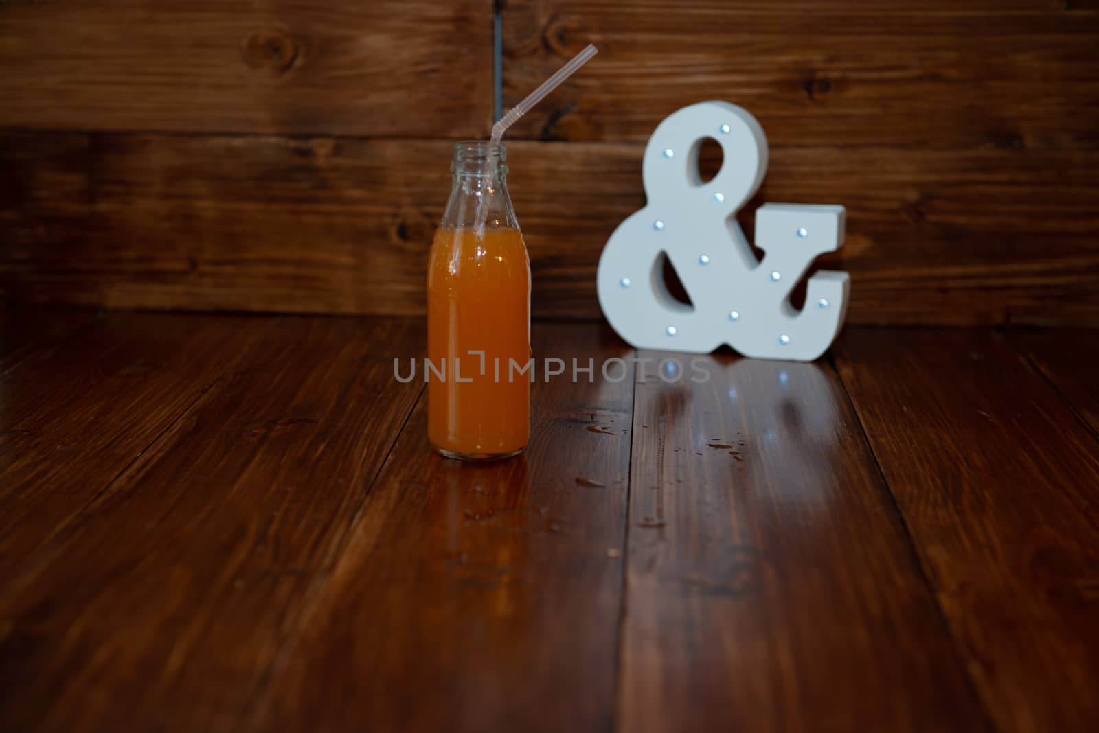 a vintage bottle of freshly squeezed juice on a wooden background and a glowing ampersand by marynkin