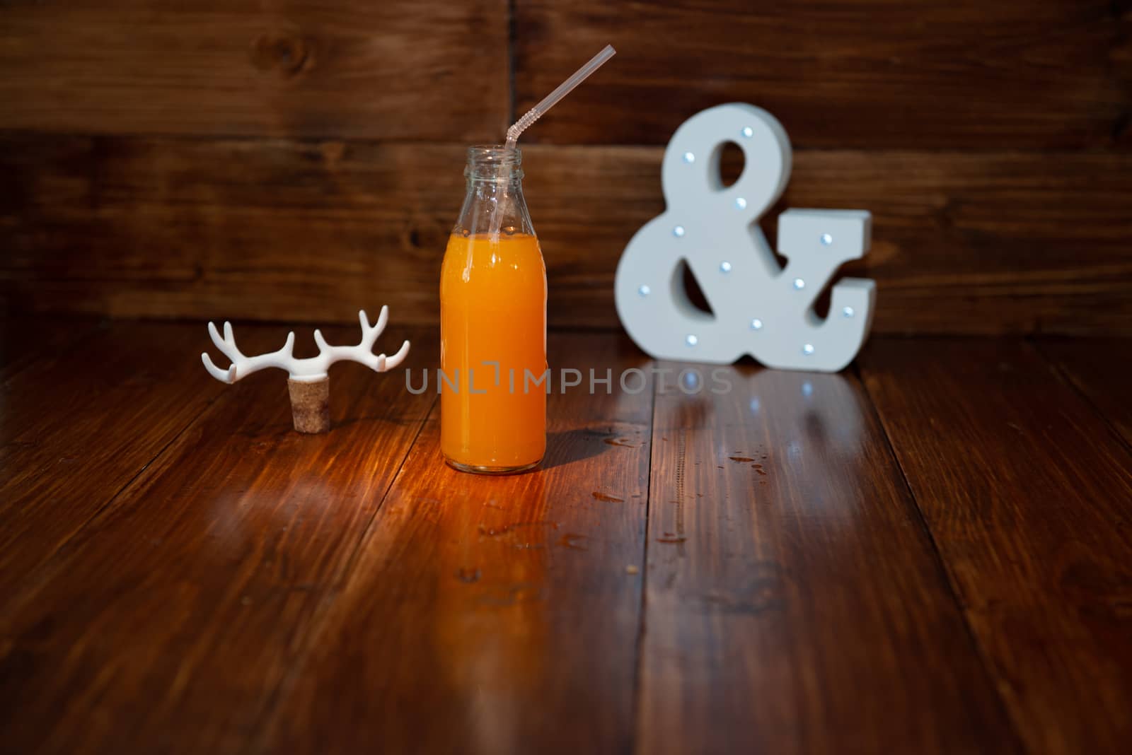 a vintage bottle of freshly squeezed juice on a wooden background and a glowing ampersand. Near wine cork decorated with deer antlers.