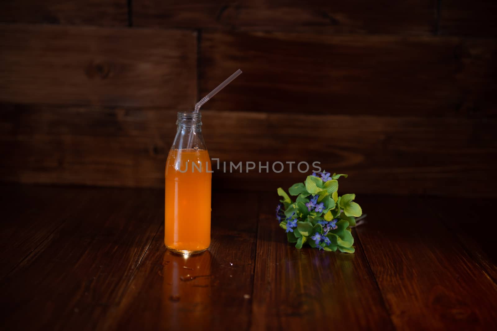 vintage bottle with juice, straw and flowers on wooden table.