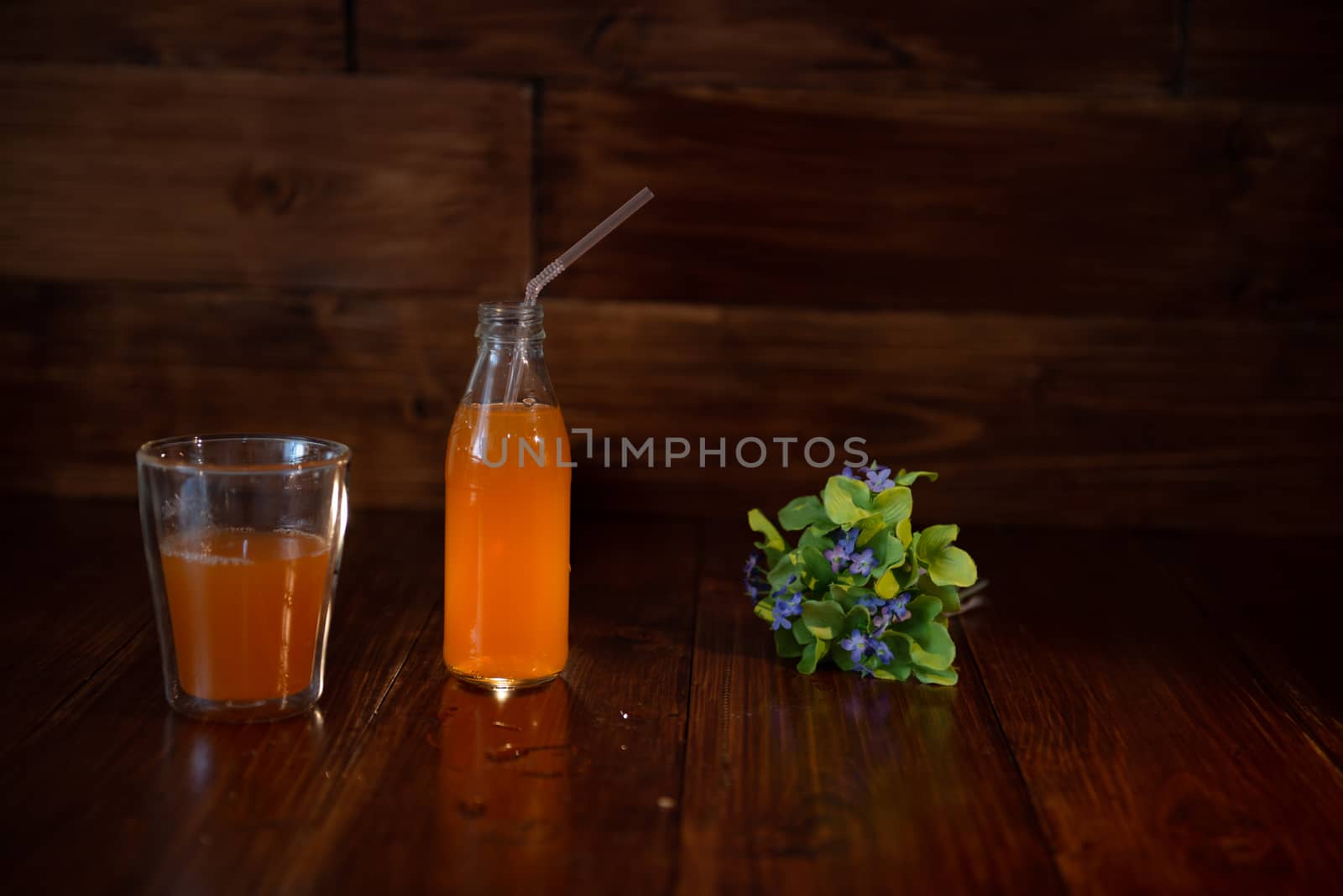 vintage bottle with juice, straw and flowers on wooden table.