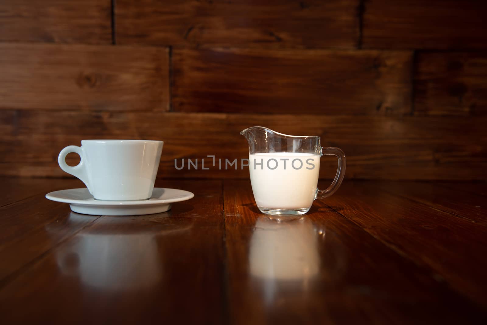 milk in glass milk jug with white cup and reflection from a wooden table by marynkin