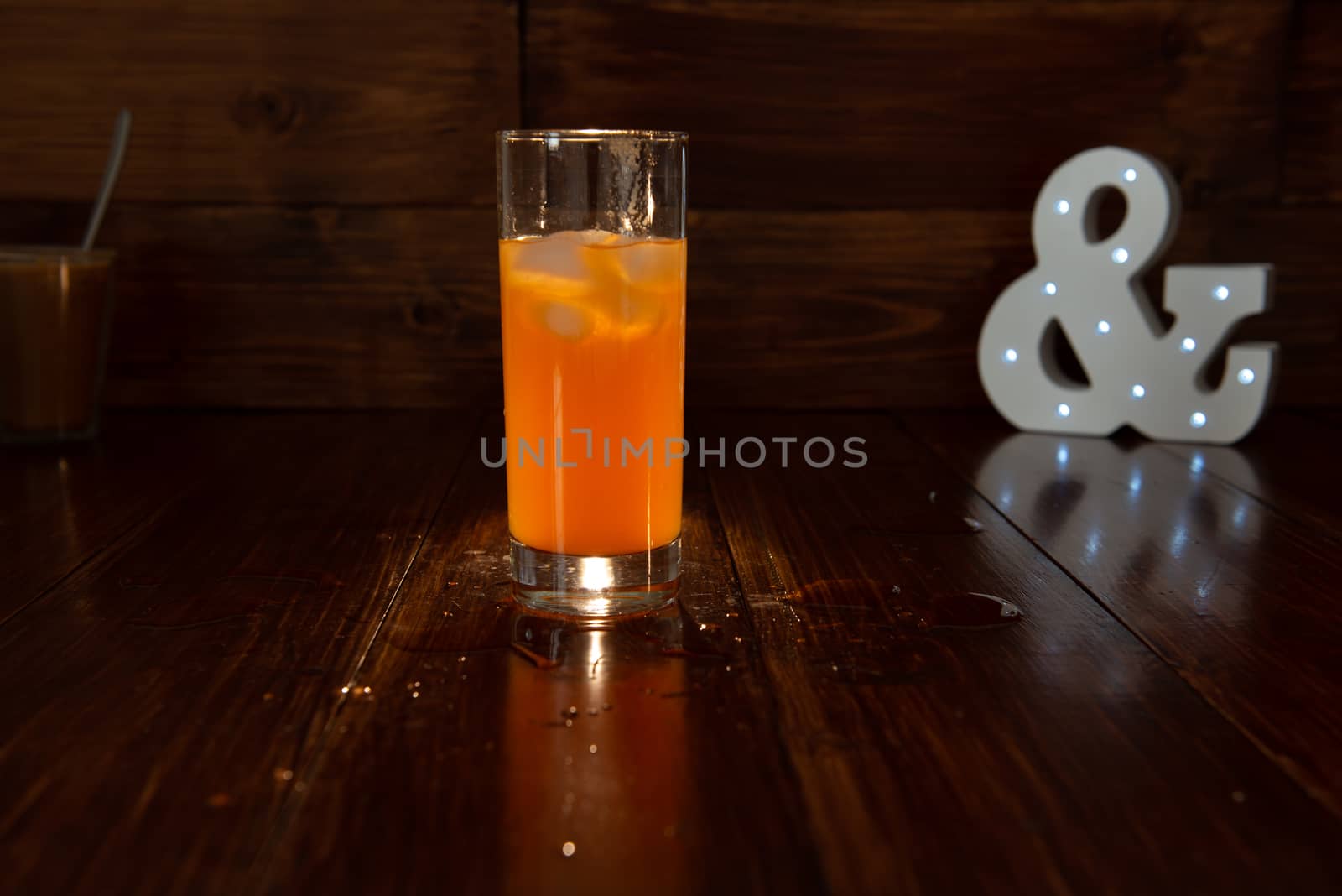 a glass of freshly squeezed juice on a wooden background and a glowing ampersand by marynkin