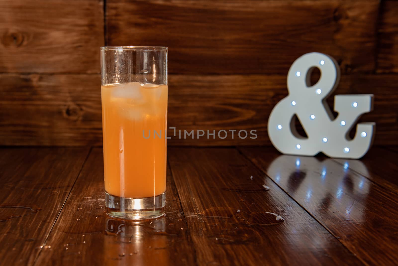 a glass of freshly squeezed juice on a wooden background and a glowing ampersand by marynkin