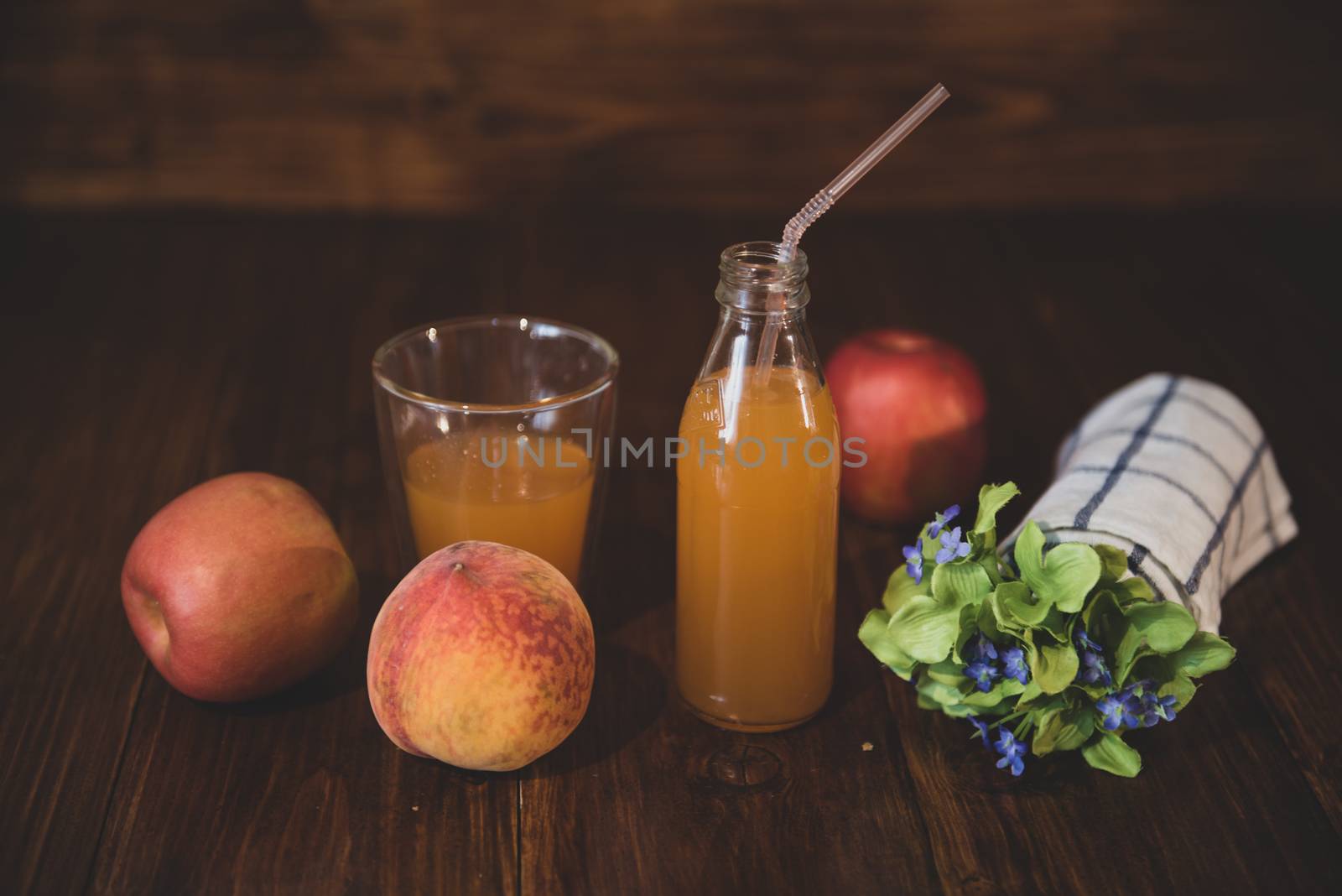 Fresh juice in bottle on wooden table with flowers and fruits