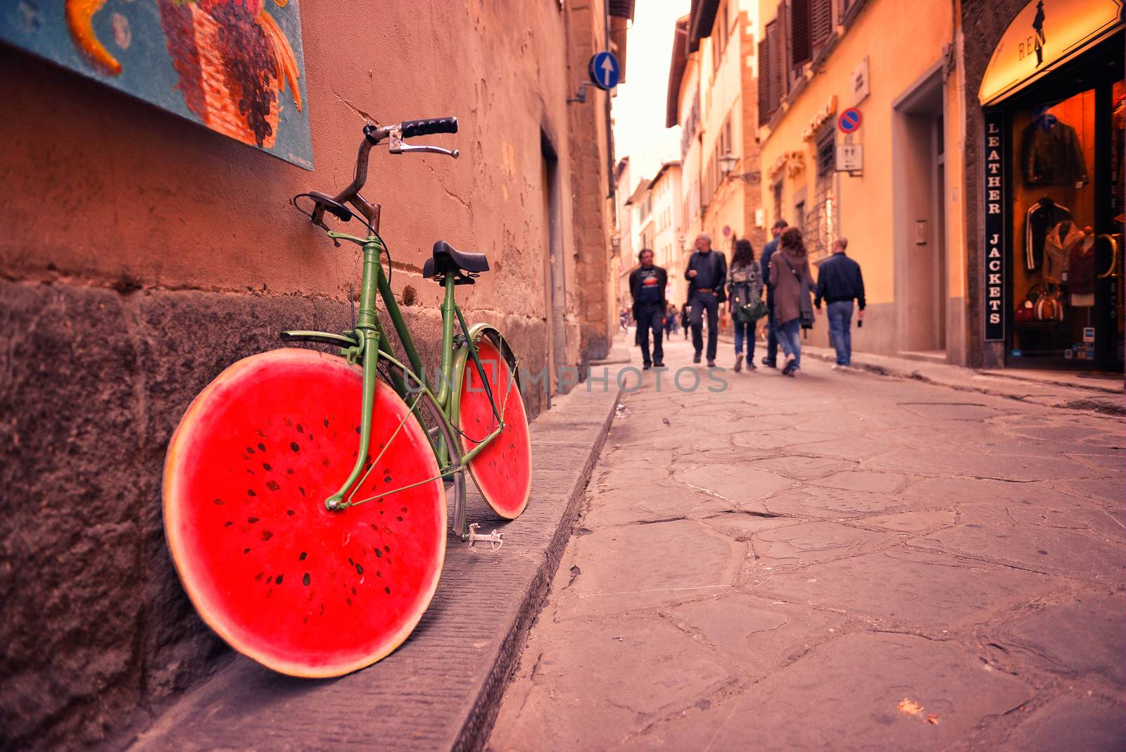 Old bicycle with watermelon wheels near the wall of the building.