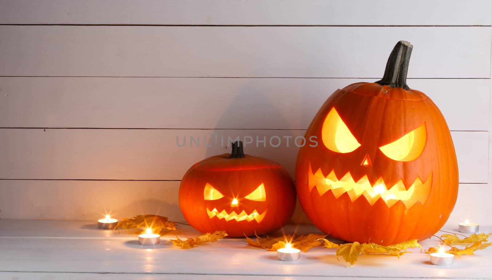 Two Halloween pumpkin heads jack o lantern and candles on wooden background