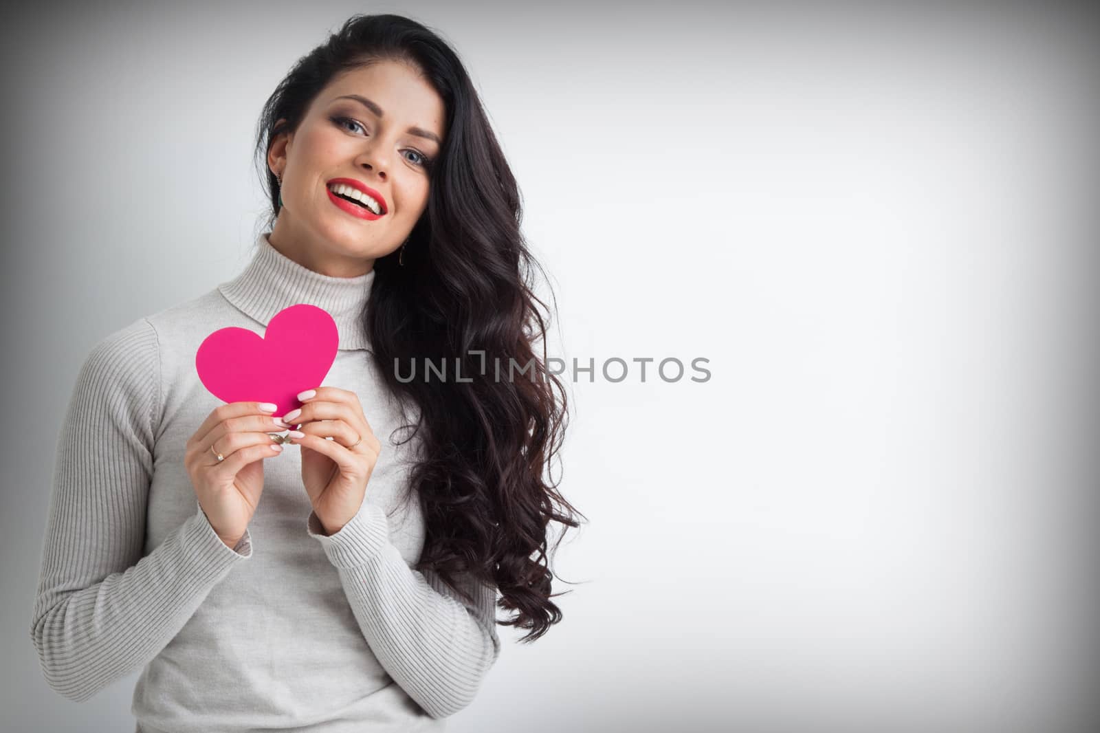 Beautiful young brunette woman holding pink paper heart , looking at camera
