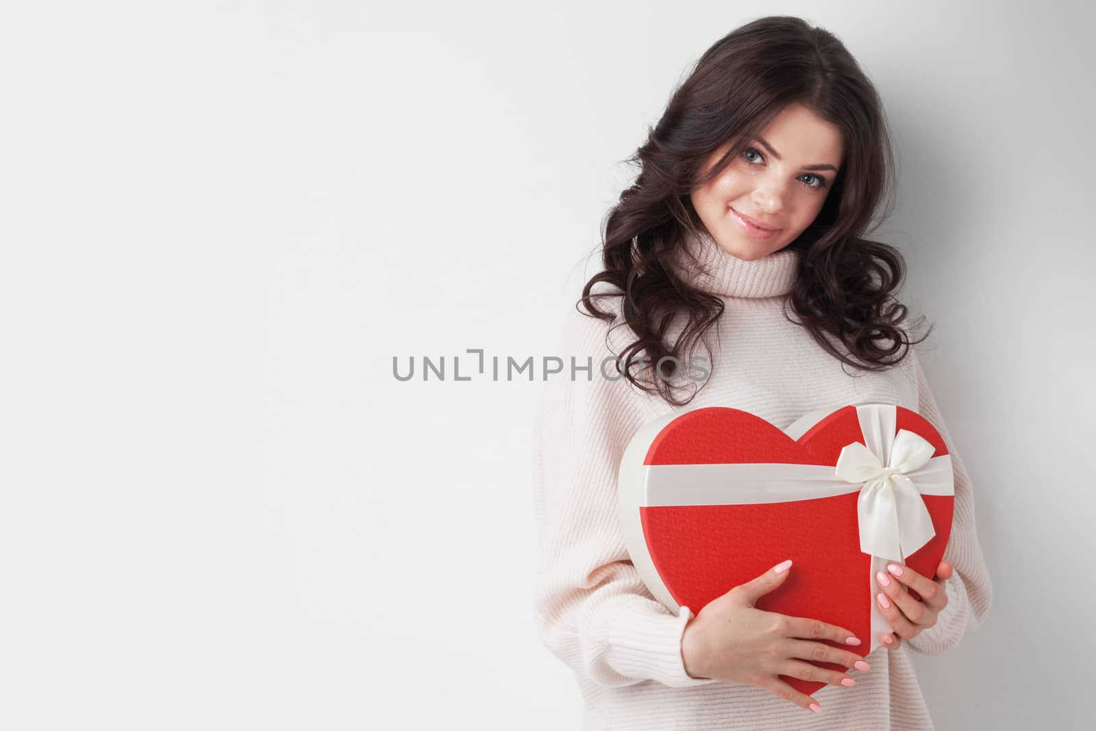 Young girl with red heart-shaped gift box on white background