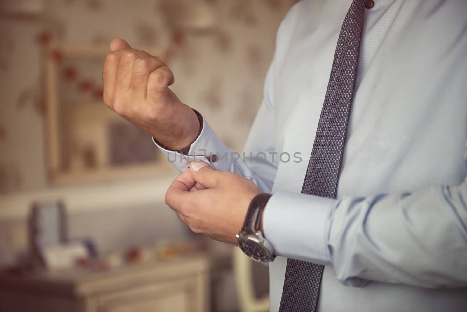 Male hands fixing stylish silver cufflinks on blue shirt cuffs sleeves in formal suit by marynkin