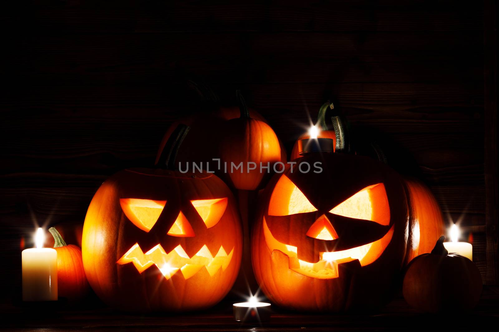 Three Halloween pumpkins head jack o lantern and candles on wooden table background