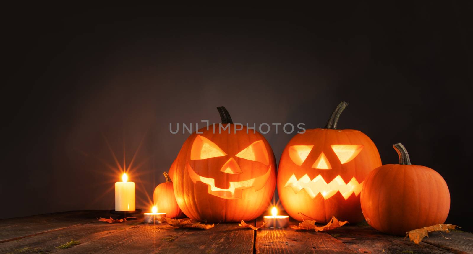 Three Halloween pumpkins head jack o lantern and candles on wooden table background