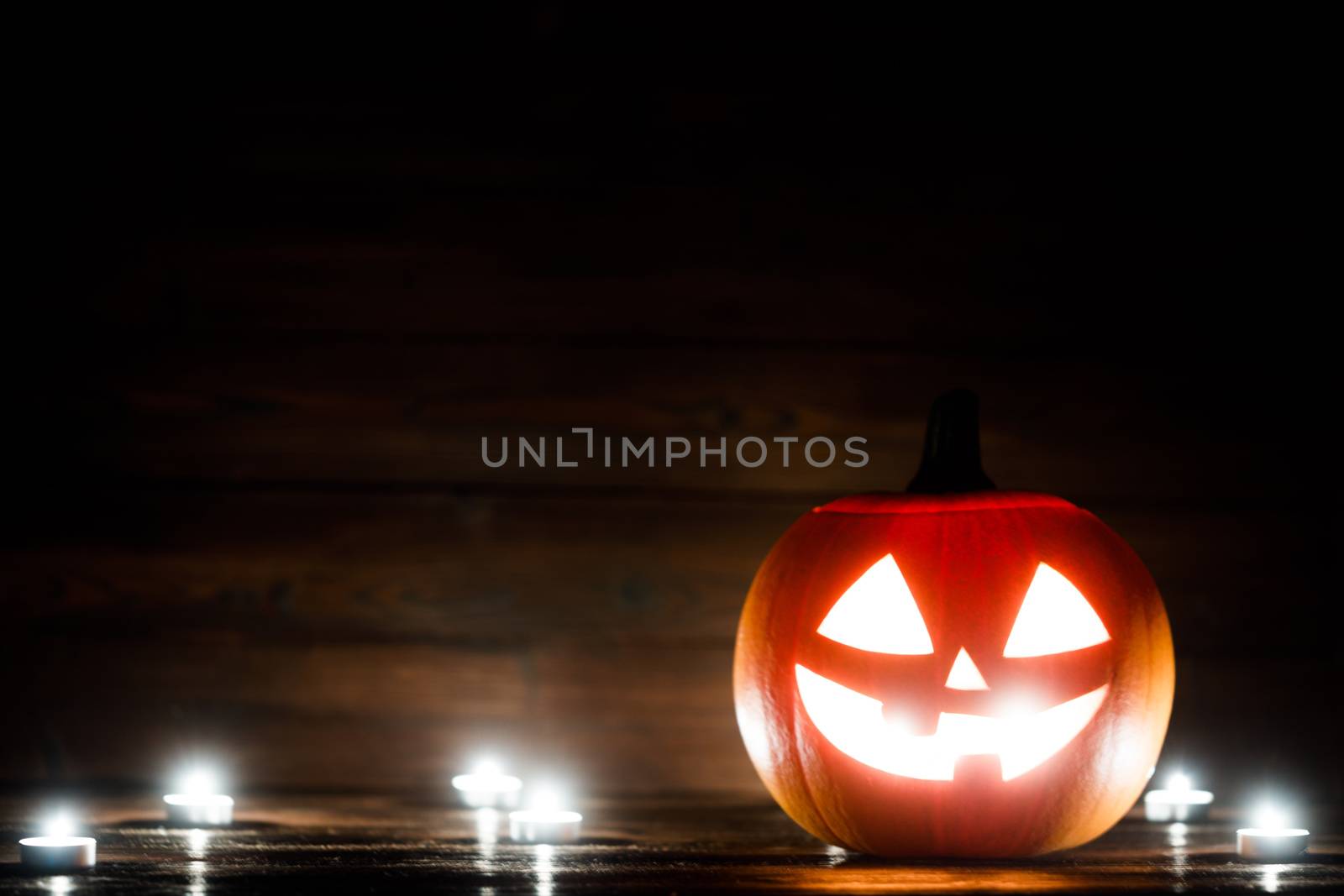 Halloween pumpkin head jack o lantern and candles on wooden background