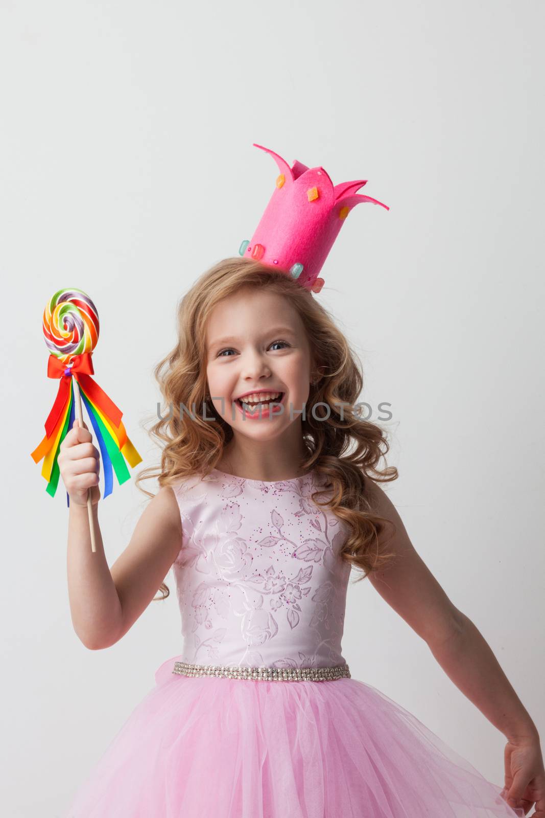 Beautiful little candy princess girl in crown holding big lollipop and smiling