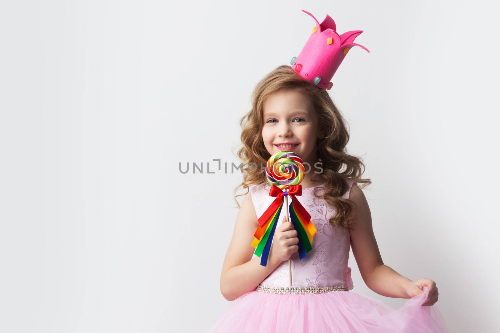 Beautiful little candy princess girl in crown holding big lollipop and smiling