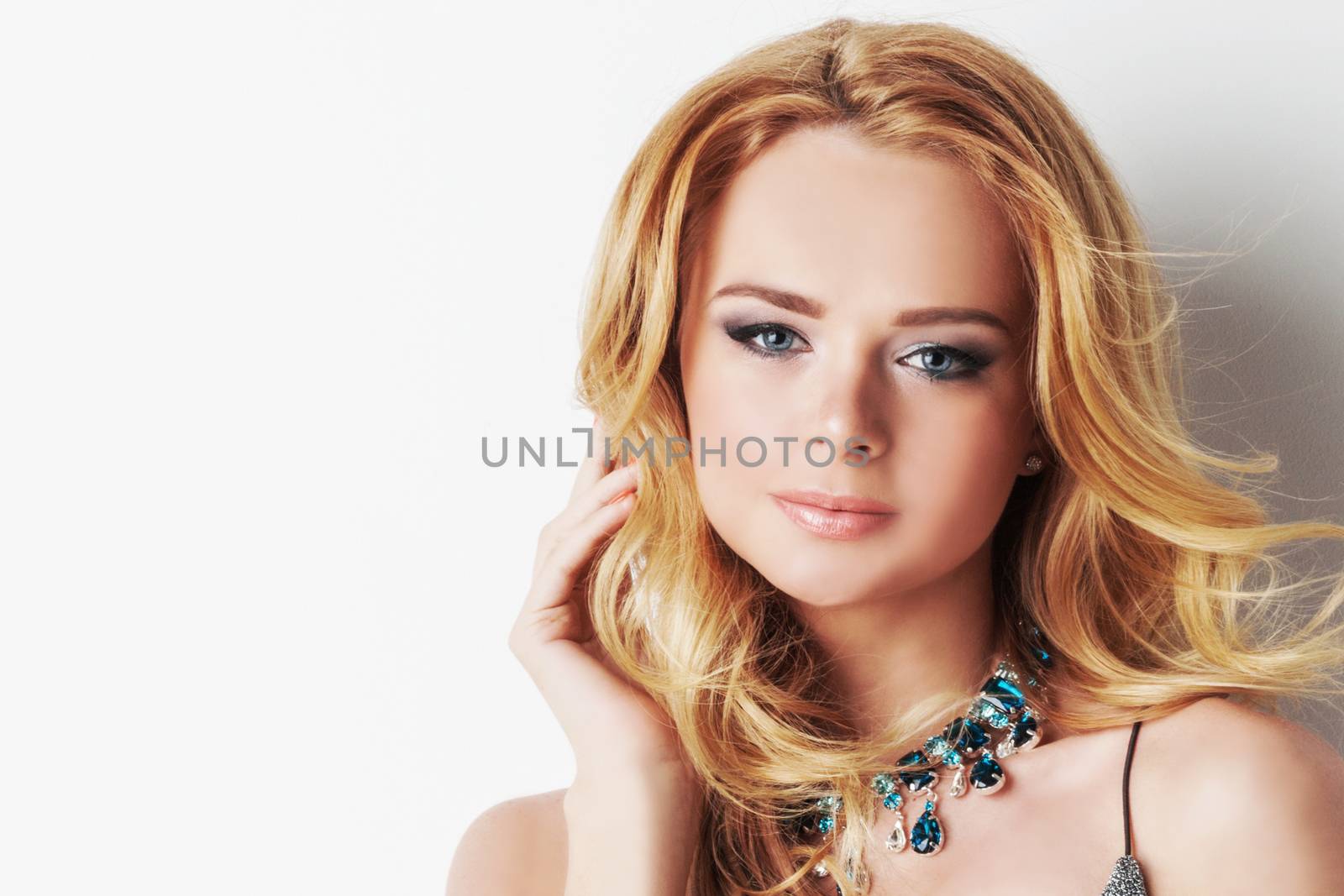 Portrait of beautiful woman with blonde curly hair and necklace of blue precious stones close up