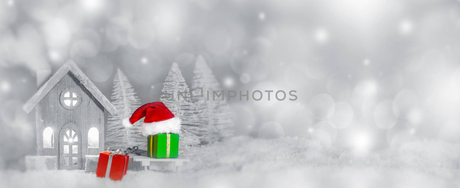 Christmas card with cozy small decorative house , gifts and Santa Claus cap on sleigh on snow over fairy tale winter fir forest background and falling snow . New Year design postcard . Copy space for text