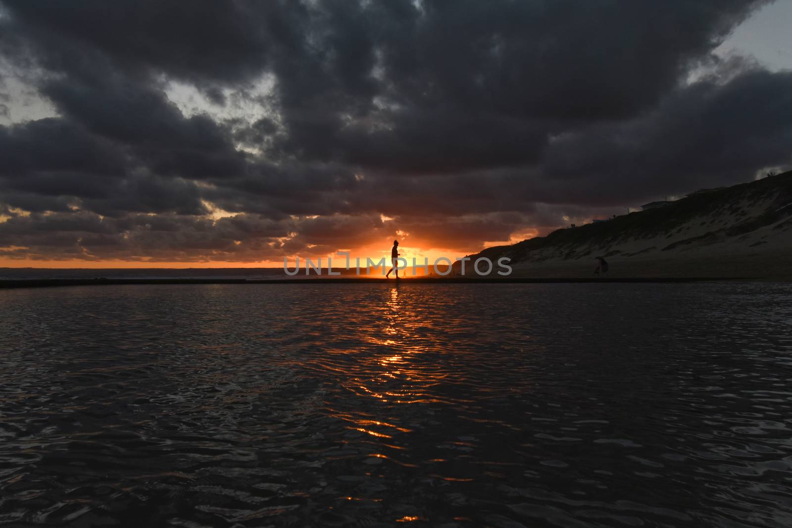 Silhouette of a woman in the sunset over tide pool water surface, Mossel Bay, South Africa