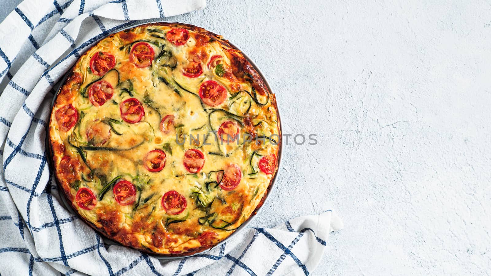 Zucchini pie on gray background, copy space right. Top view of delicious savory pie with zucchini, tomatoes, herbs and cheese. Idea and recipe for healthy baking and lot to harvest of zucchini