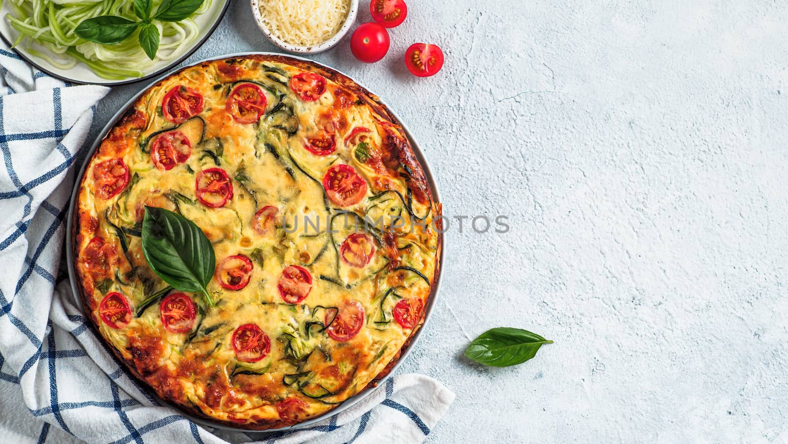 Zucchini pie on gray background, copy space right. Top view of delicious savory pie with zucchini, tomatoes, herbs and cheese. Idea and recipe for healthy baking and lot to harvest of zucchini