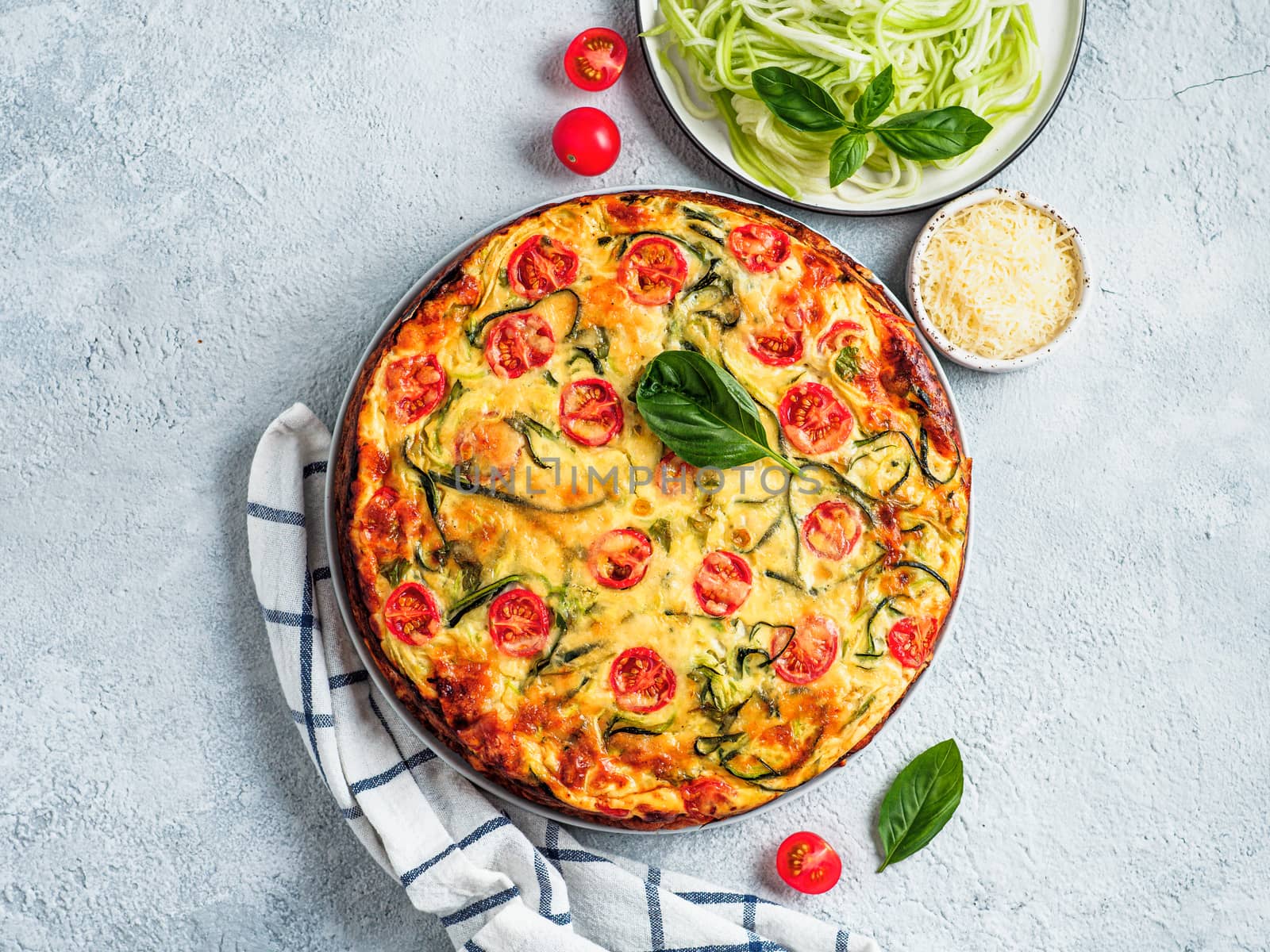 Zucchini pie on gray background, copy space. Top view of delicious savory pie with zucchini, tomatoes, herbs and cheese. Idea and recipe for healthy baking and lot to harvest of zucchini