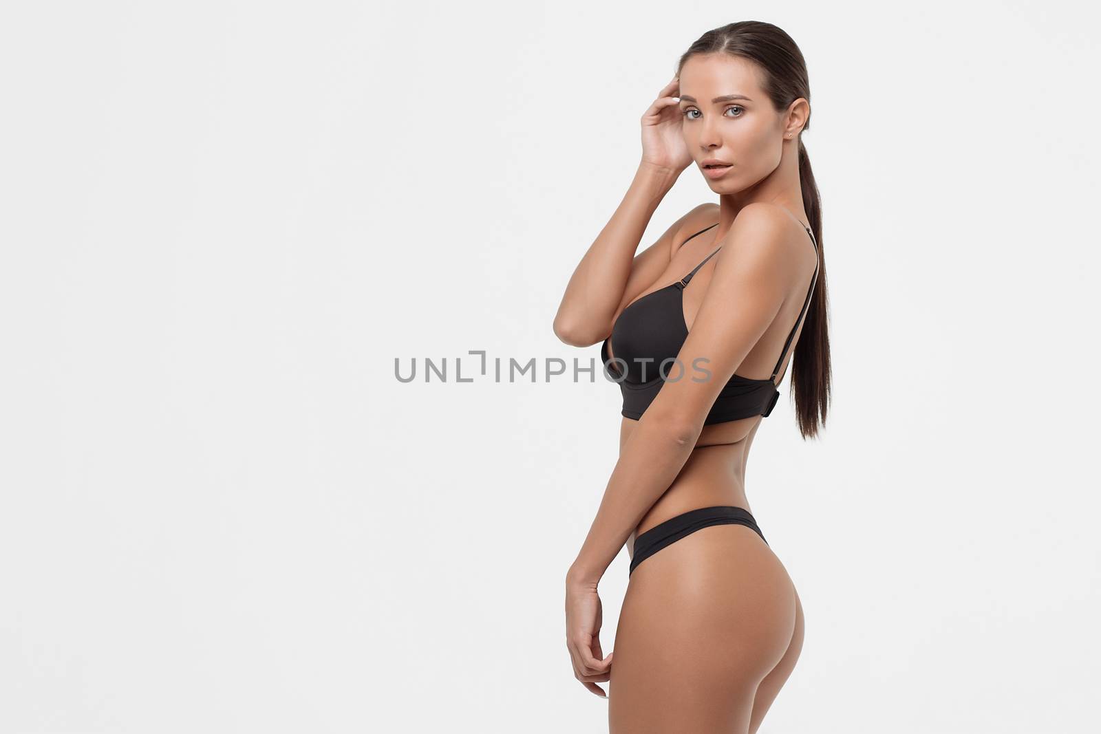 Side view of seductive young woman in black underwear standing with eyes closed in studio