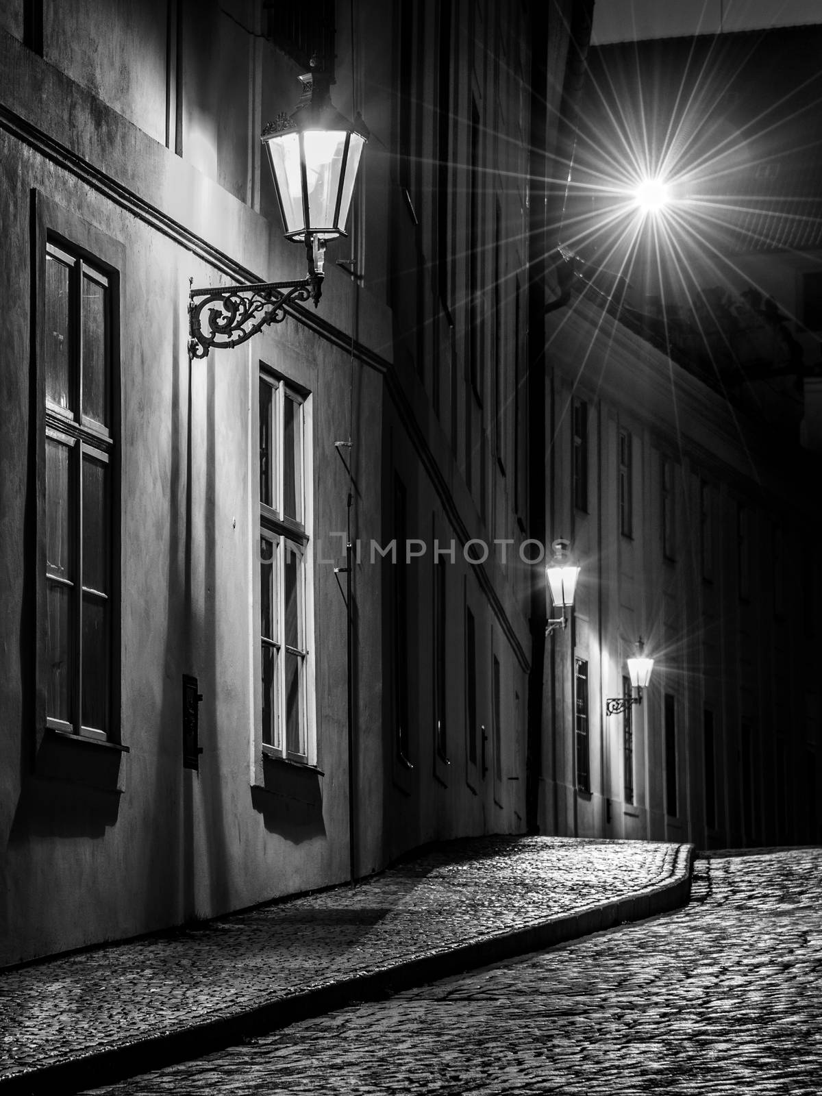 Narrow cobbled street illuminated by street lamps of Old Town, Prague, Czech Republic. Black and white image.