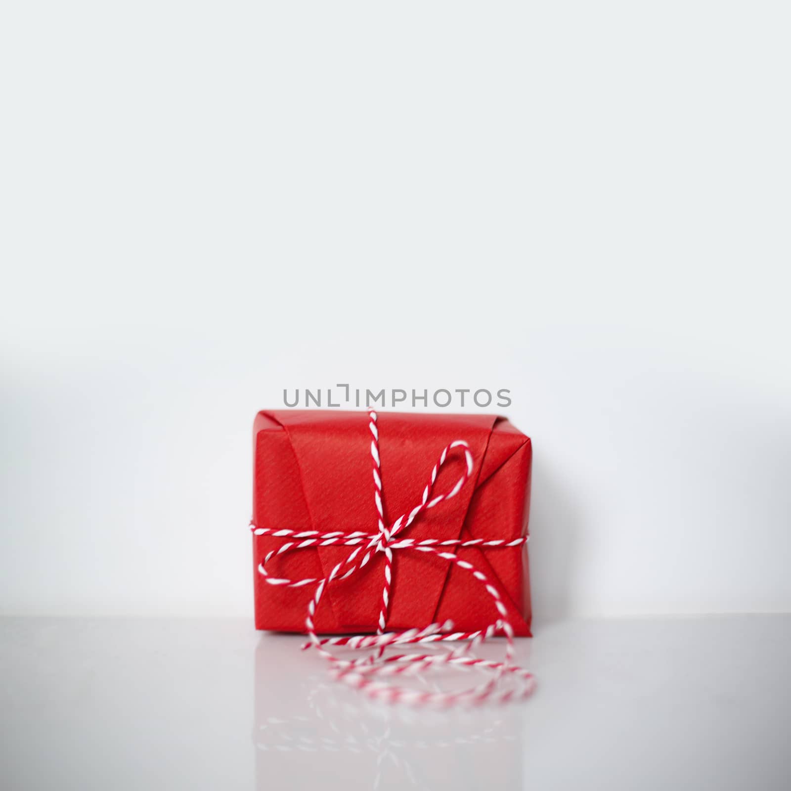 Christmas gift box wrapped in red paper and bow of dtriped rope on white background