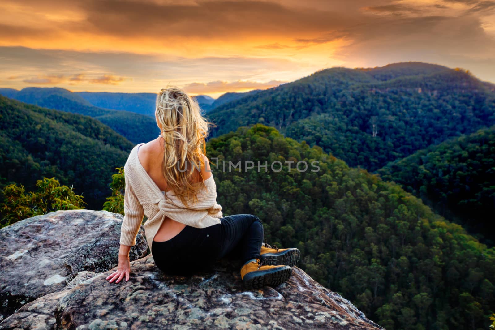 Woman sitting on a rock overlooking the valley, mountain gazing as the sun sets