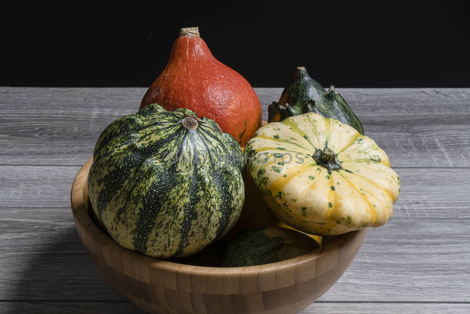 Some small pumpkins in a wooden bowl on the table