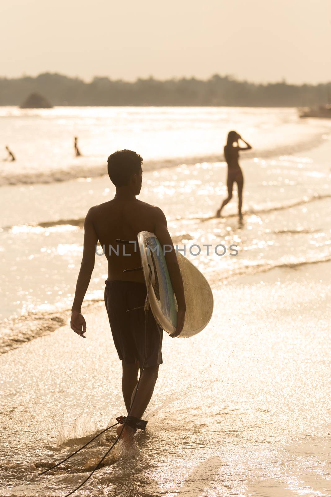 Man walking at tropical beach of Midigama, Sri Lanka at sunsen with surf board in his hands. by kasto