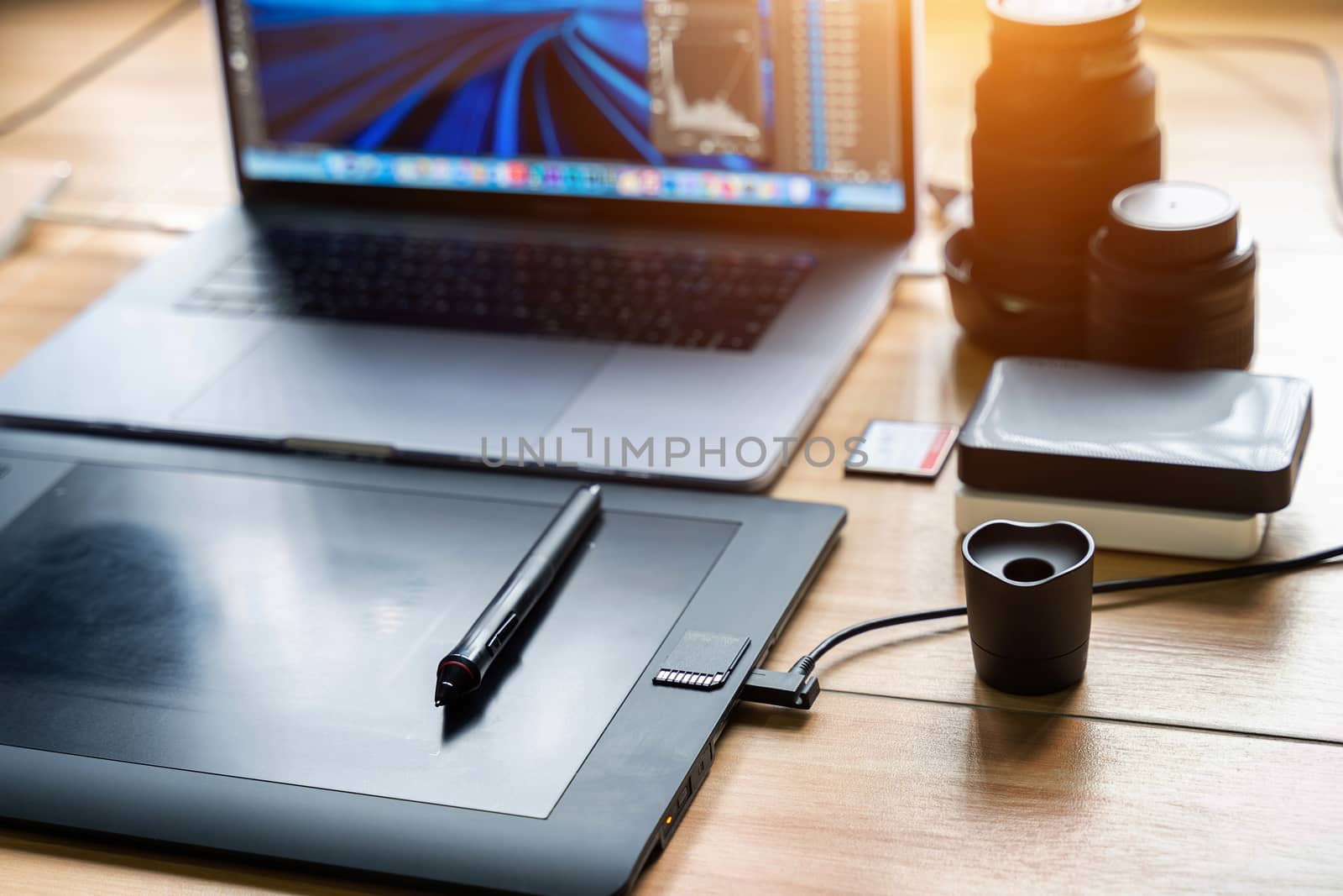 Drawing tablet and laptop computer, harddisk, memory card, camera lens on table. Photographer concept.