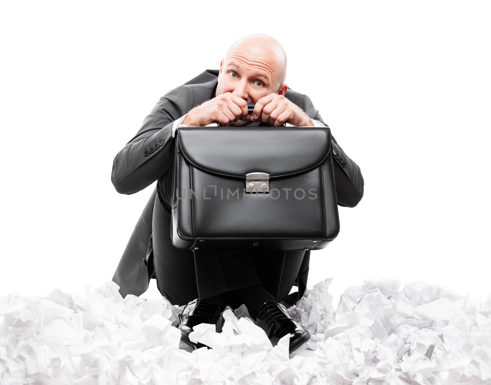 Business problems and failure at work concept - unhappy scared or terrified businessman in depression hand holding briefcase sitting down floor on crumpled torn paper document heap white isolated