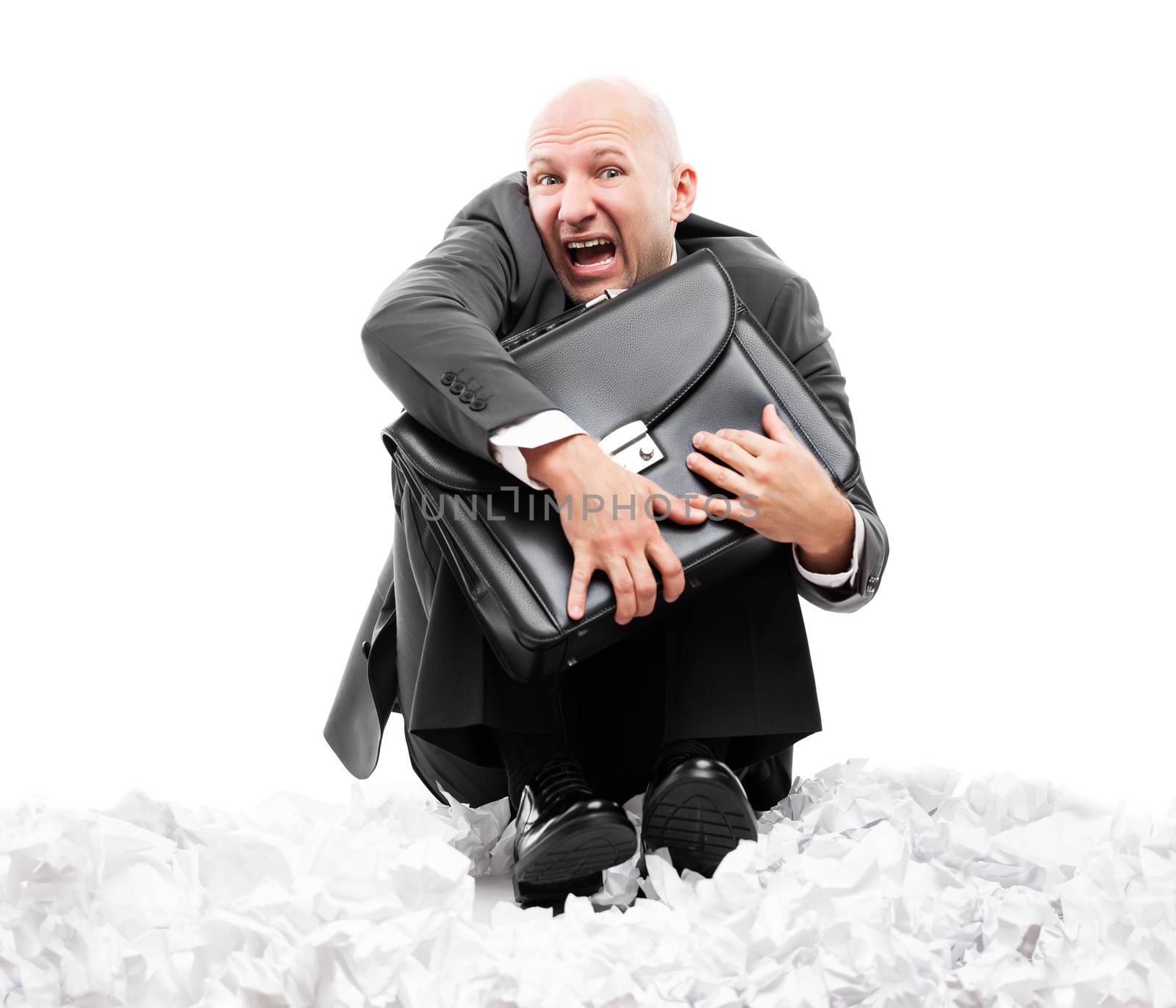 Business problems and failure at work concept - unhappy scared or terrified businessman in depression hand holding briefcase sitting down floor on crumpled torn paper document heap white isolated