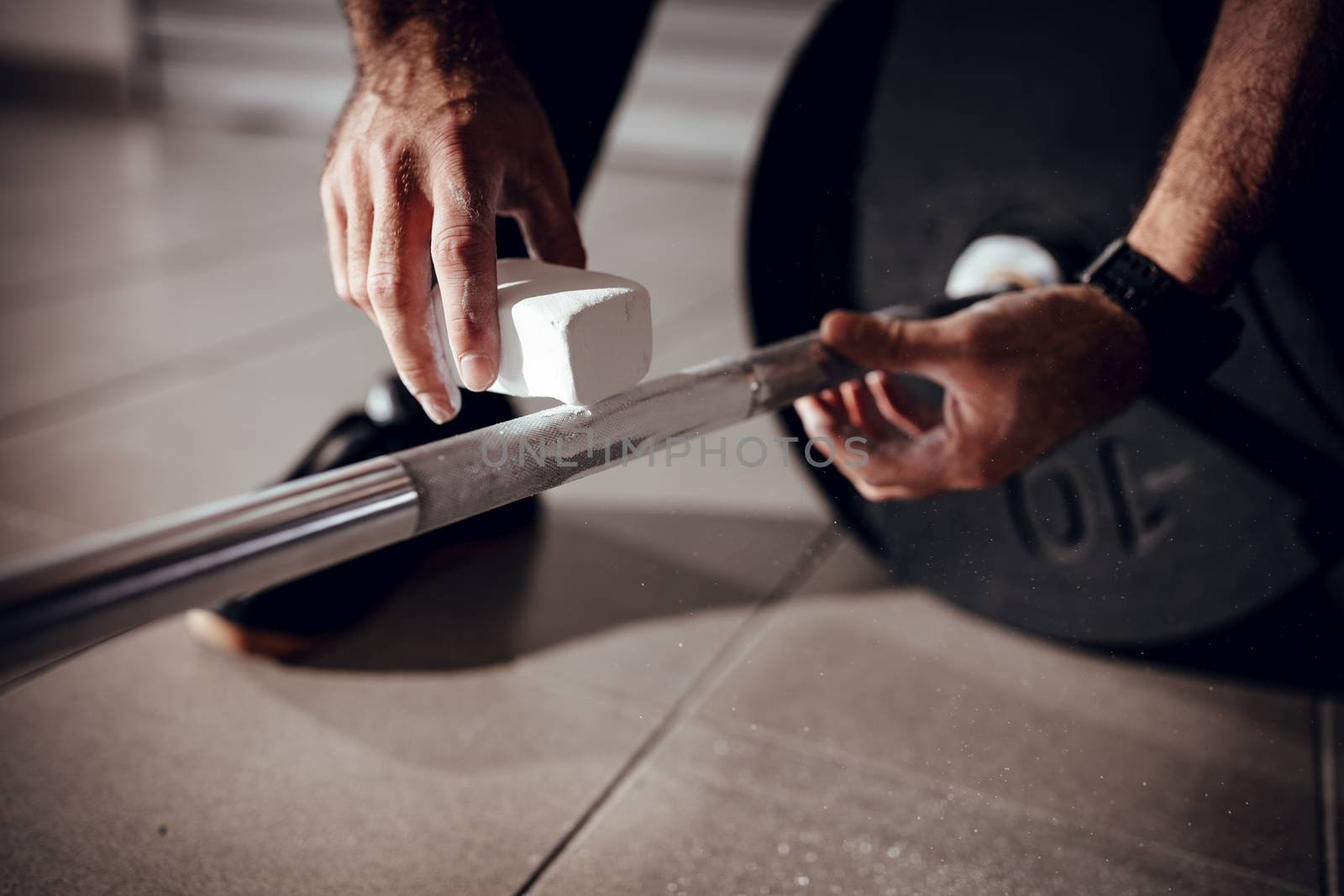 Close-up of a strong man's hands with magnesium powder getting ready to weightlifting at the garage gym.