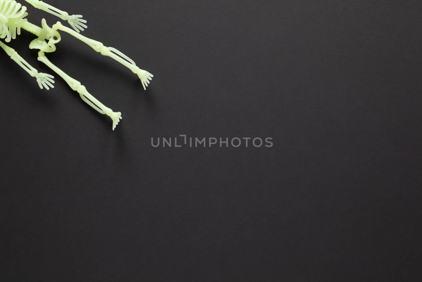 Halloween holiday flat lay. White fluorescent skeleton on black background with copy space. Minimal style. Horizontal. Trick-or-treat concept by ALLUNEED