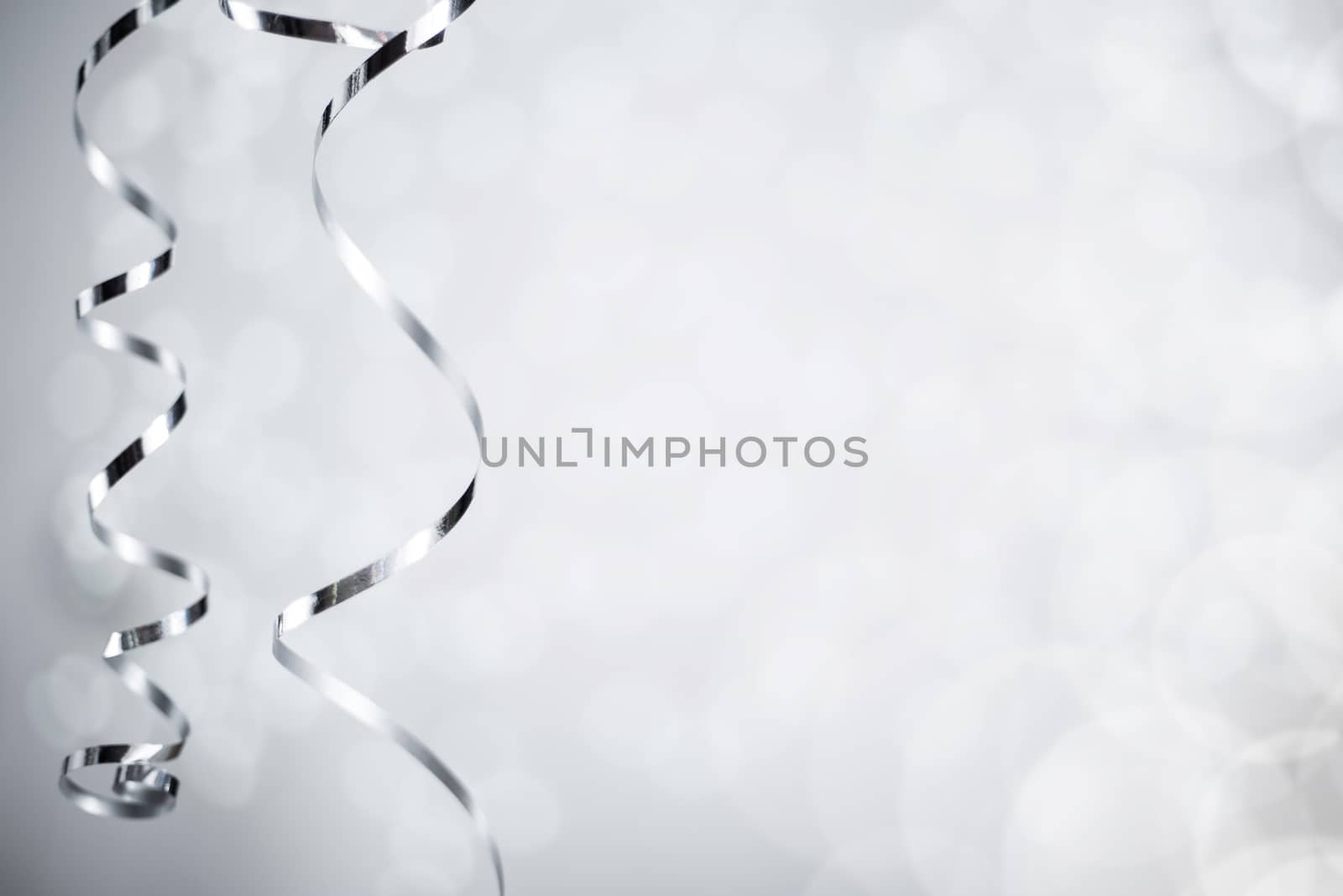 Silver Christmas new year curly streamer ribbon over glittering bokeh lights background with copy space for text