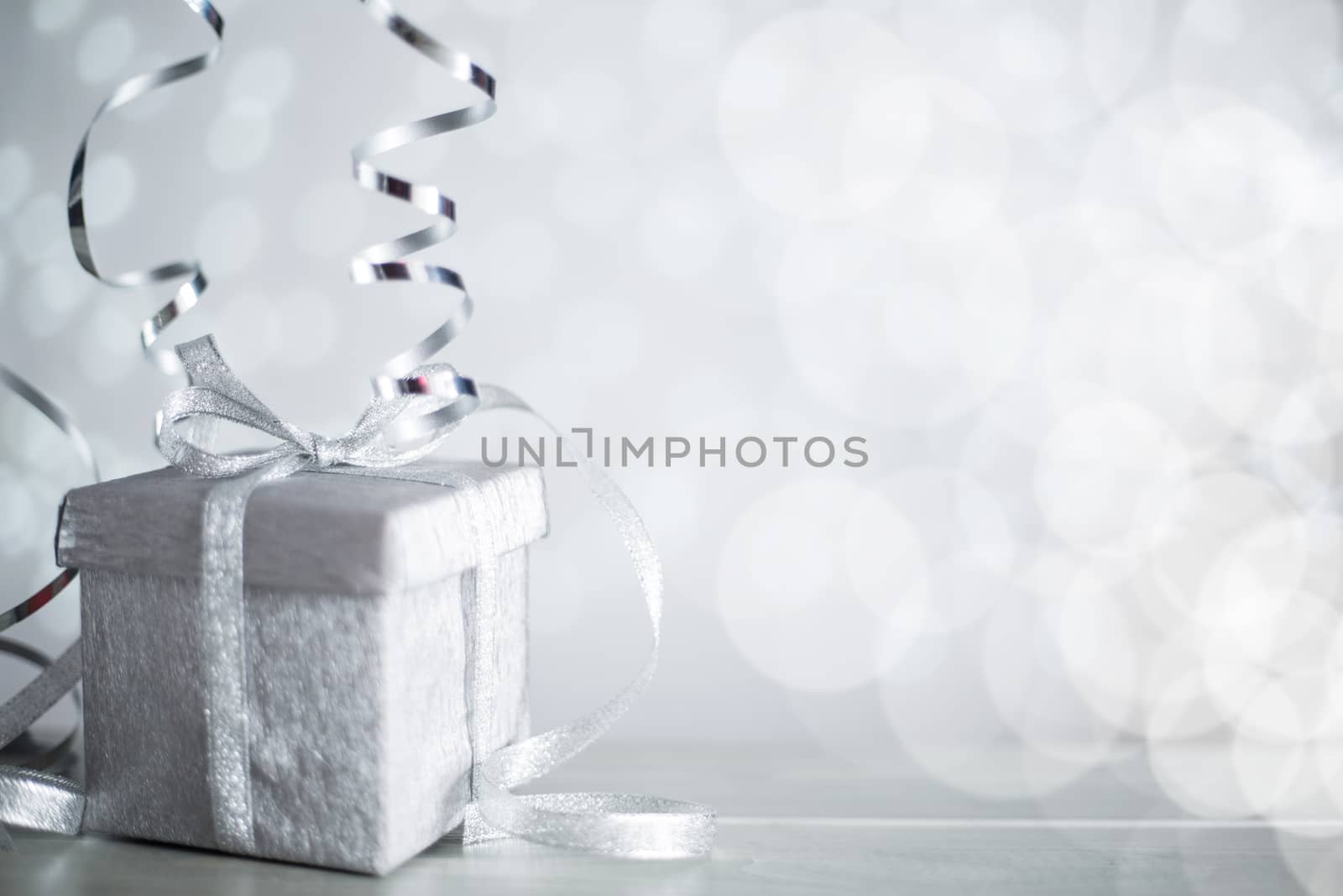 Silver Christmas new year gift with curly streamer ribbon bow over glittering bokeh lights background with copy space for text