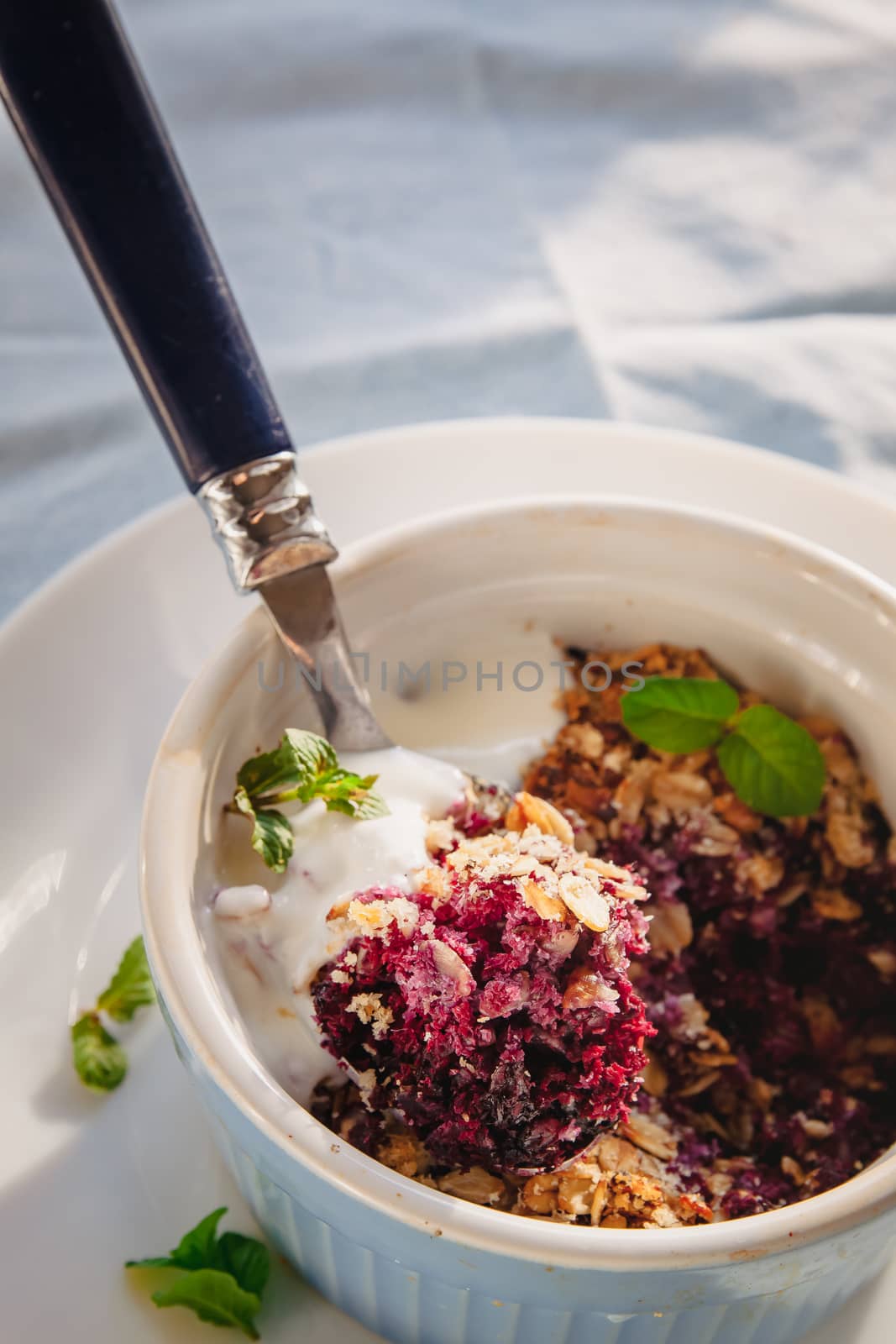 baked oat-blueberry crumble with mint in a white and blue plate on a rustic linen tablecloth. Save the space, top view. The concept of healthy proper nutrition for breakfast, vegetarianism