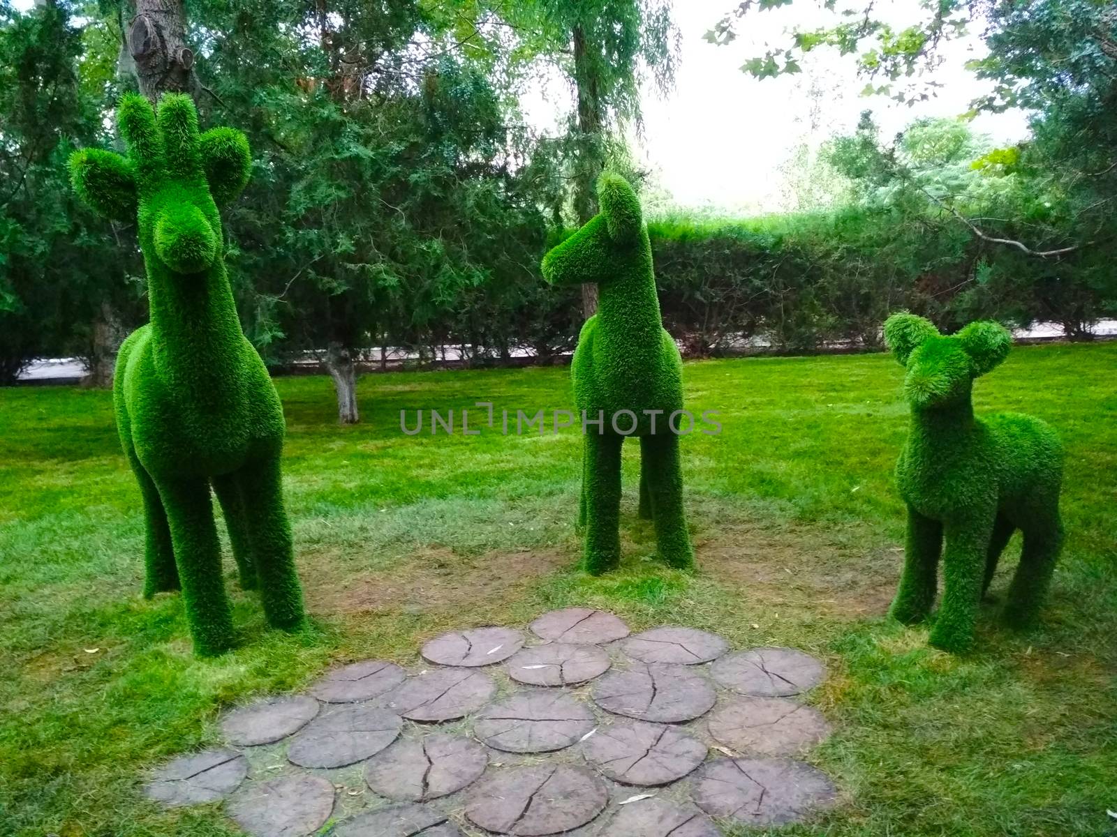 
Sculptures of three deer in profile in the Park green on the background of trees.