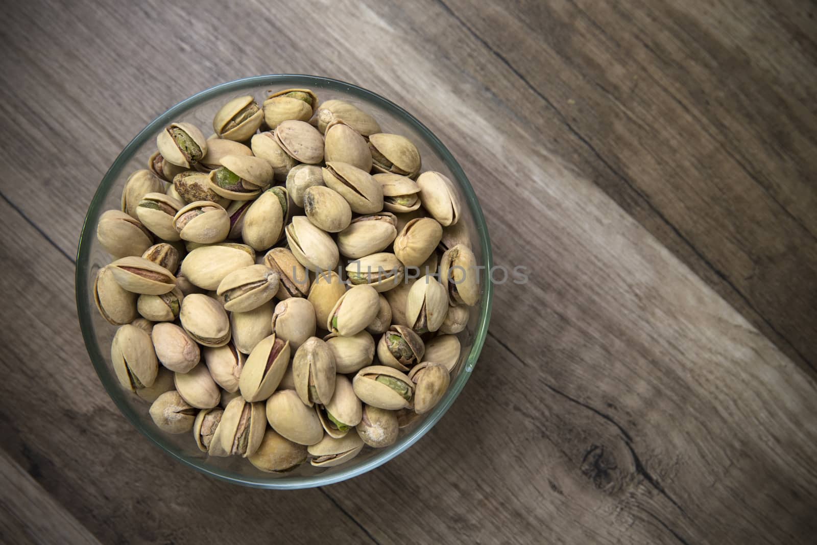 Glass bowl of pistachios on a wooden table as background