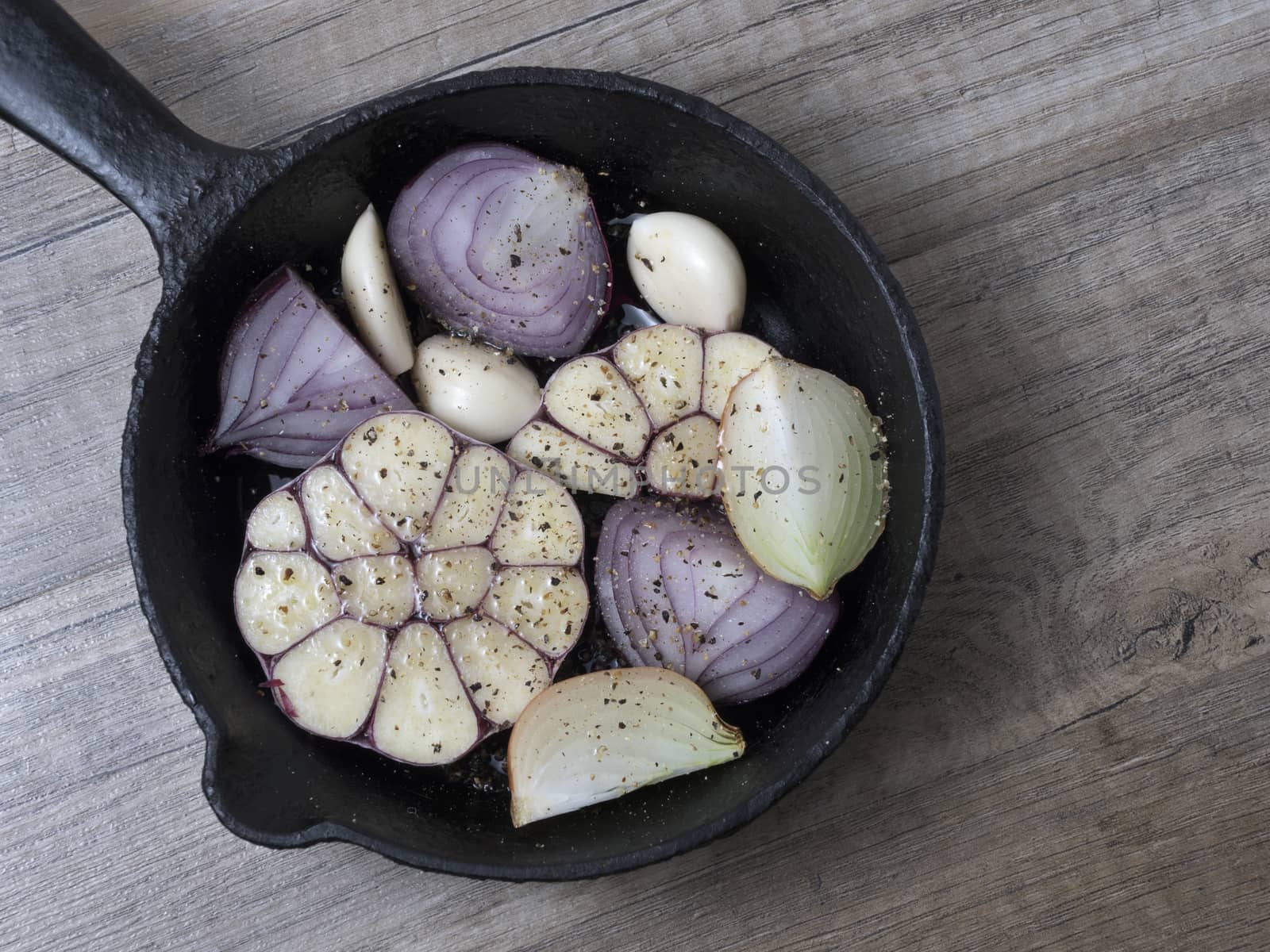 Slices of garlic, red and yellow onion in a frying pan with spices, on wooden background. Top view. 