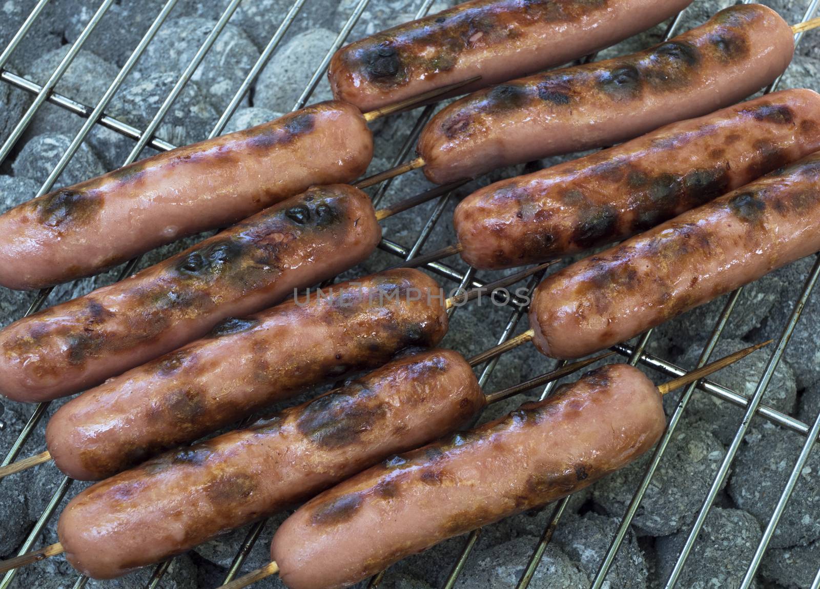 Grilling Sausages on Bamboo Sticks on Barbecue Grill Close Up