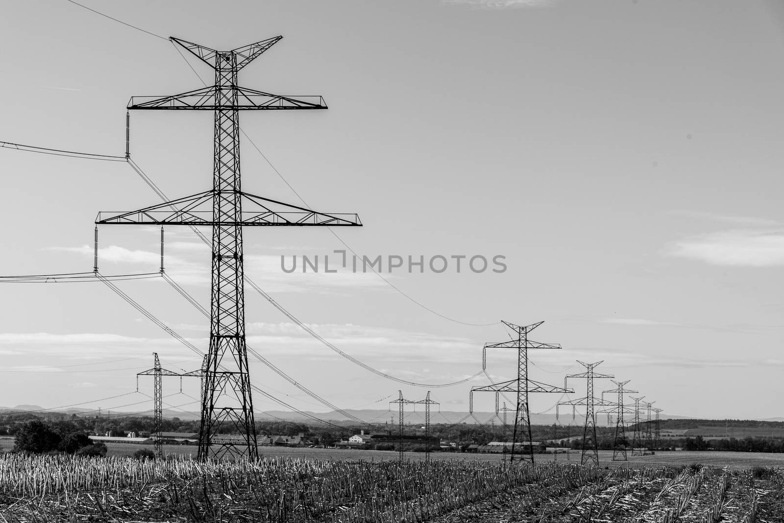 Line of transmission towers, or electricity pylons, in the rural landscape. Black and white image.