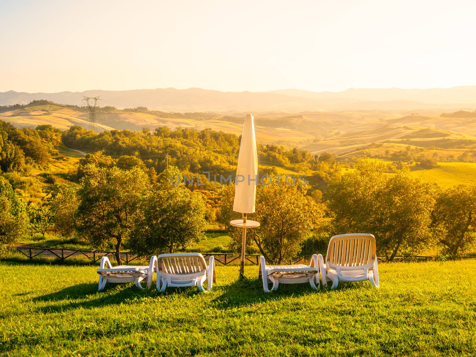 Beautiful rest place with umbrellas and sunbeds in Tuscan landscape. Evening summer sunset. Italy.