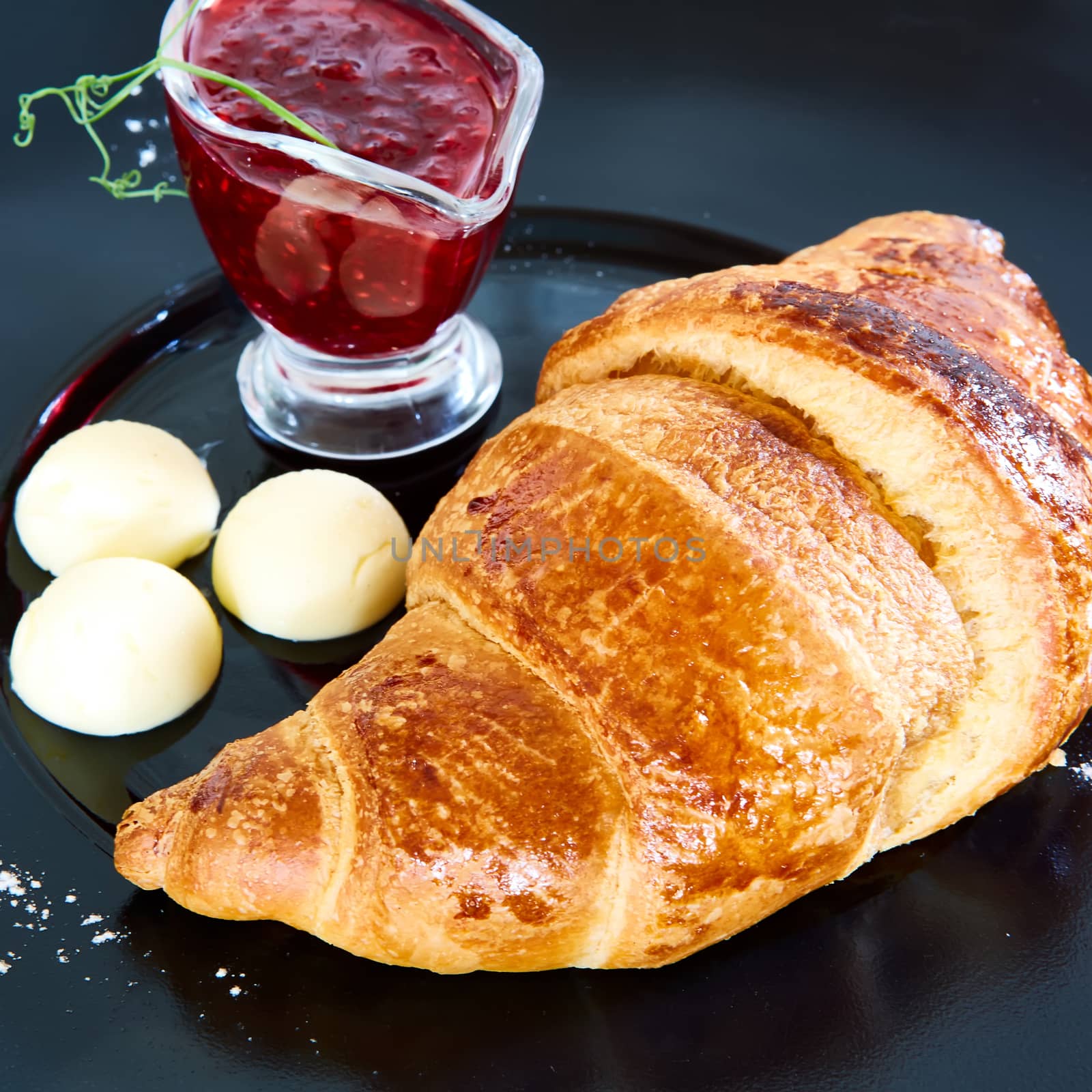 Closeup of butter, jam and fresh croissants.