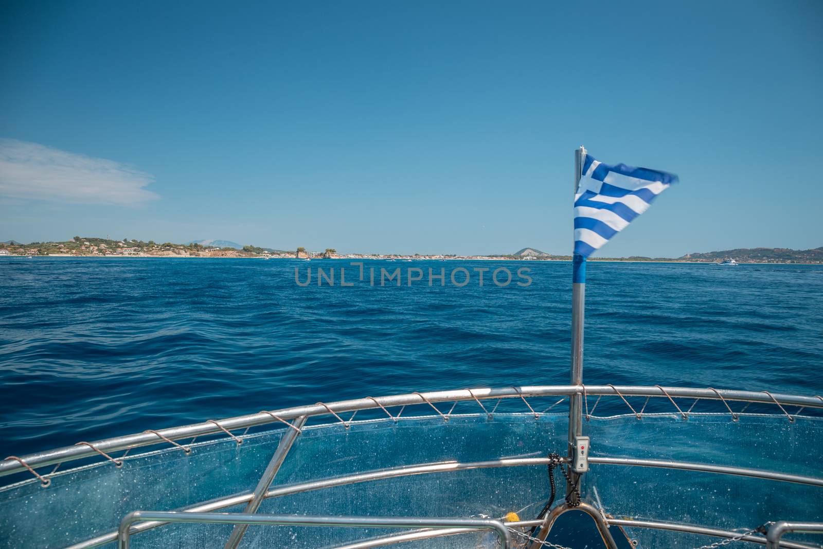 Flag of Greece waving over the see on cruise sheep in front of beautiful coastline