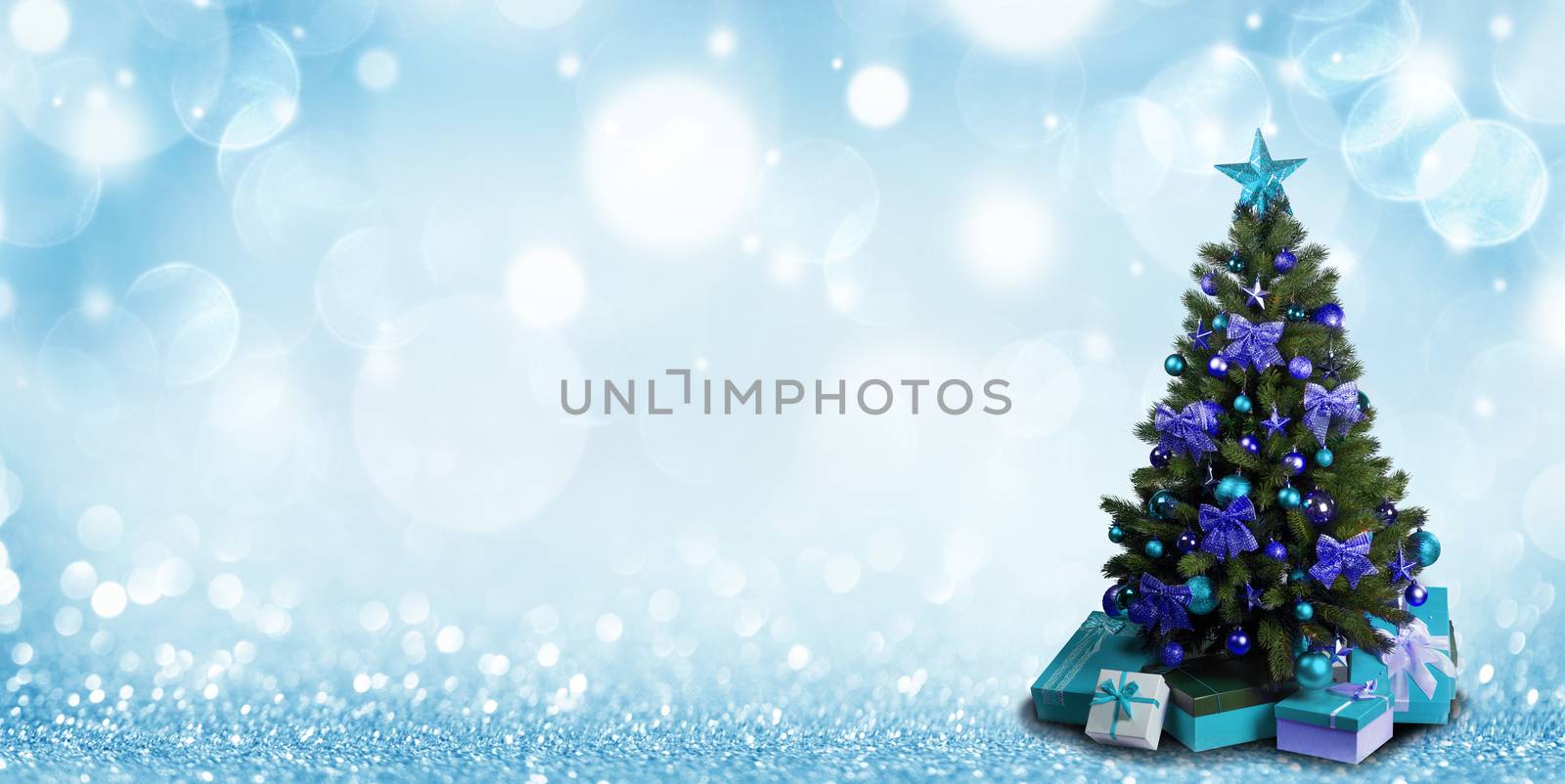 Fully decorated christmas tree with blue and green baubles and bows and presents on glitter bokeh background