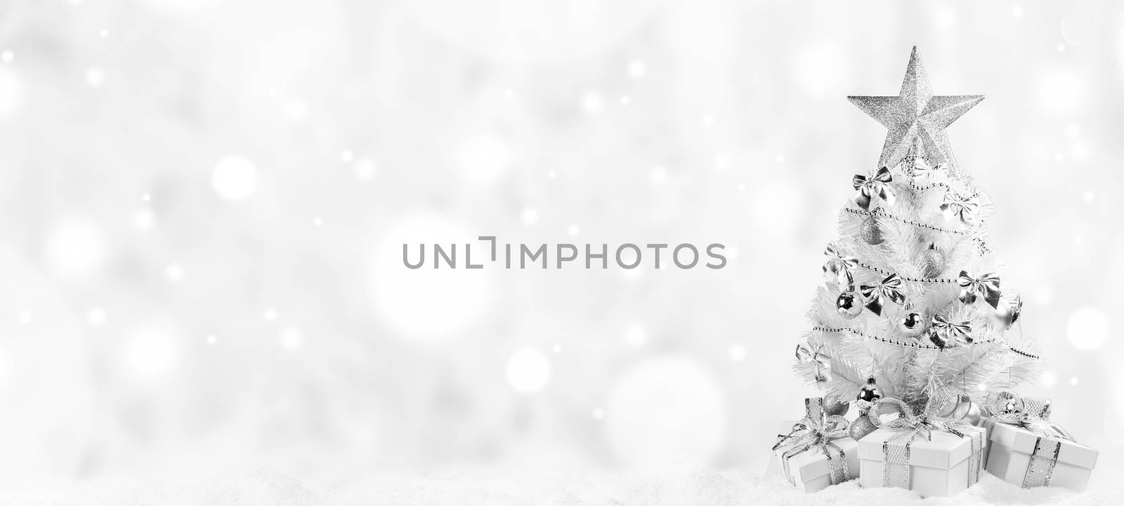 White christmas tree with silver decorations and gifts on snow on bokeh background